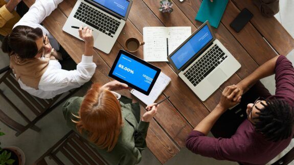 A bird's eye view of employees at a desk looking at results on a tablet and laptops.